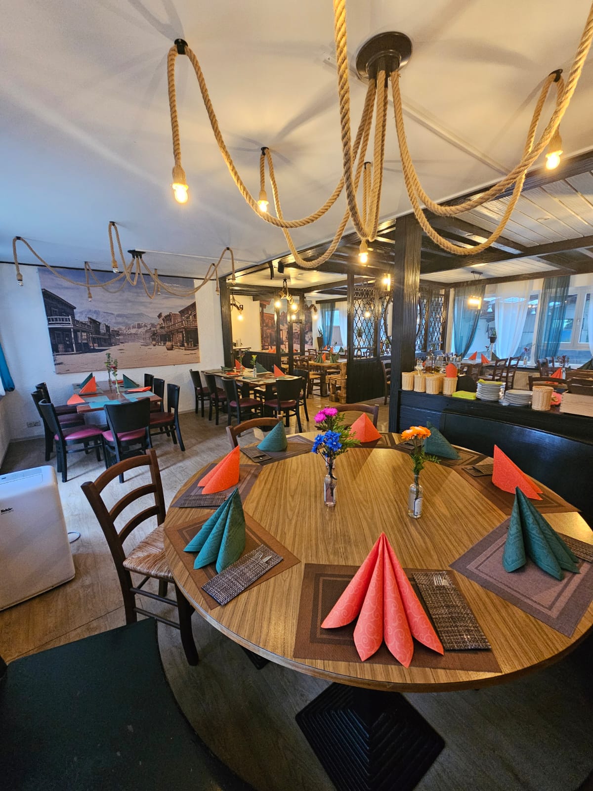 Ein runder gedeckter Holztisch mit bunten Servietten und Blumen in einem Restaurant