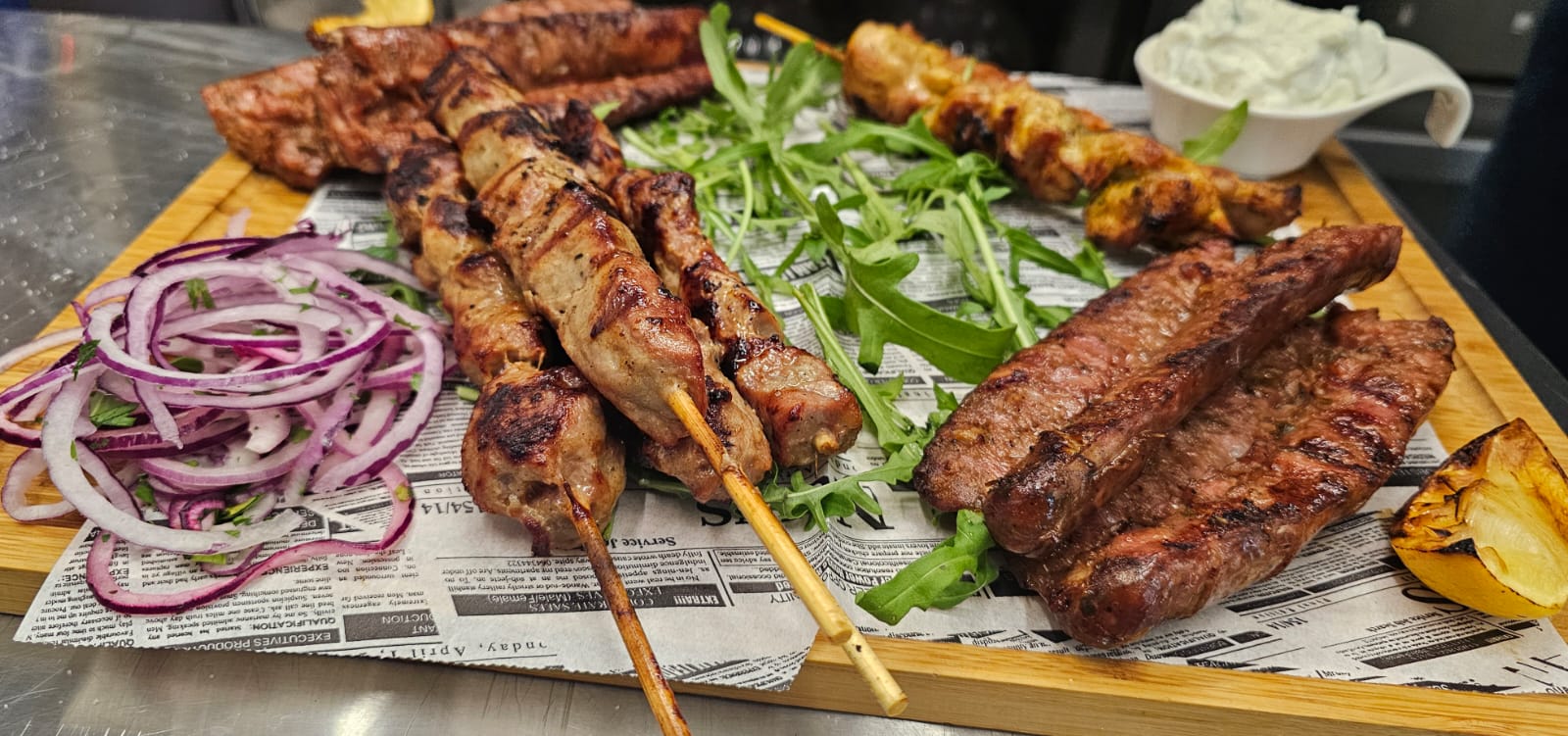 Grillspieße und Fleisch mit Röstaromen auf Holzbrett, rote Zwiebeln und Rucola